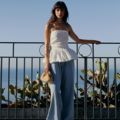 Mulher com top branco e calças largas de ganga junto a corrimão com cactos ao fundo