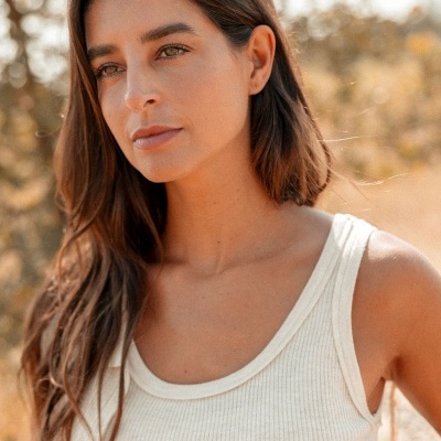 Mulher com camisola branca de alças, cabelo castanho e fundo de natureza