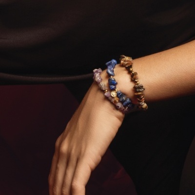 Pulso com 3 pulseiras de pedras naturais coloridas em fundo escuro