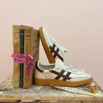 Sapatilhas brancas com riscas castanhas e livros antigos amarrados com fita rosa numa mesa de madeira rústica