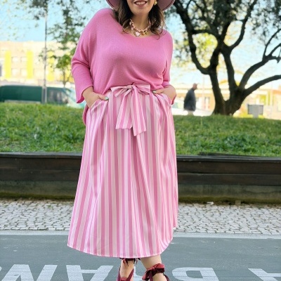 Mulher com roupa rosa e branca sorridente em ambiente urbano com árvores