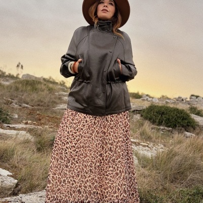 Pessoa com casaco cinza, vestido animal print e chapéu castanho em ambiente exterior