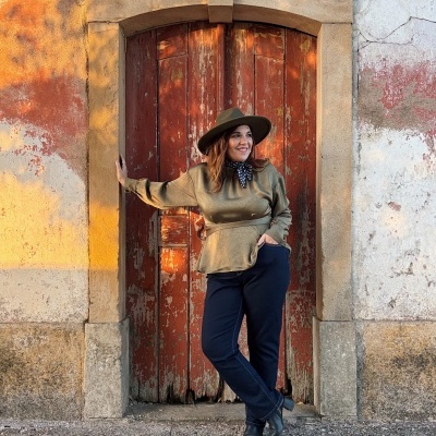 Mulher com chapéu verde-oliva e blusa verde-oliva em frente a porta vermelha desgastada