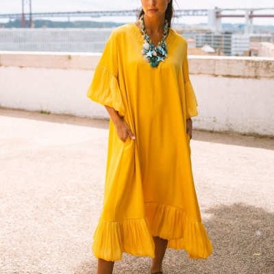 Vestido midi amarelo com folhos, colar de conchas e sandálias castanhas