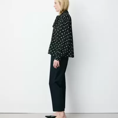 Mulher de perfil com blusa preta de bolinhas brancas, calças pretas e sapatos mule pretos