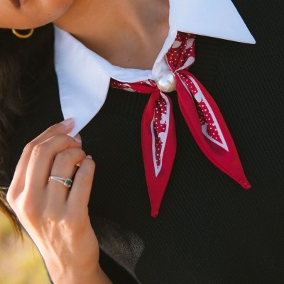 Colarinho branco com lenço vermelho e branco preso com pérola grande e anel dourado num suéter preto
