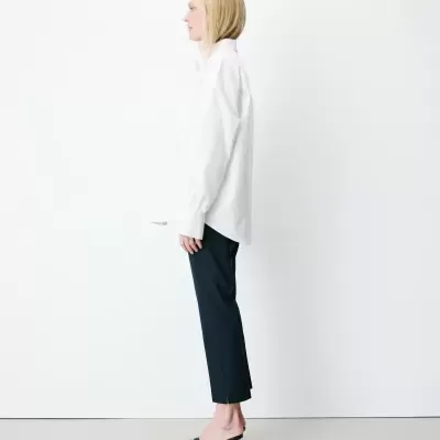 Mulher de perfil com camisa branca, calças pretas e sapatos pretos de salto alto