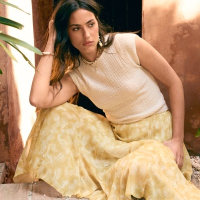 Mulher vestindo vestido amarelo com padrão floral e top creme numa pose ao ar livre