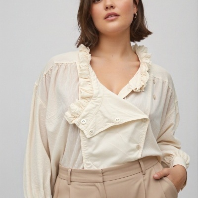 Blusa feminina bege com babados e calças bege em fundo cinza