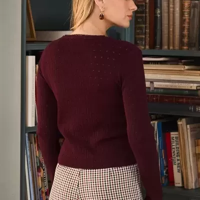 Mulher de costas com camisola vinho e calças aos quadrados em frente a estante de livros