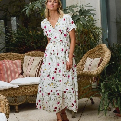 Vestido branco comprido floral com cinto usado por mulher em ambiente com móveis de vime e plantas