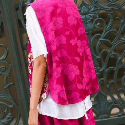 Colete e saia rosa texturizados com padrão floral, usados sobre camisa branca, com porta metálica ao fundo.