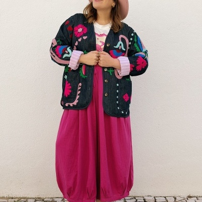 Mulher com casaco bordado colorido, saia rosa fúcsia, chapéu rosa e sandálias vermelhas em calçada