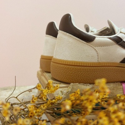 Sapatilhas em camurça bege com detalhes castanhos e sola de borracha em fundo rosa claro