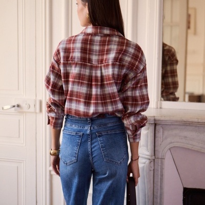 Camisa xadrez castanha e branca usada com calças jeans azuis em ambiente interior
