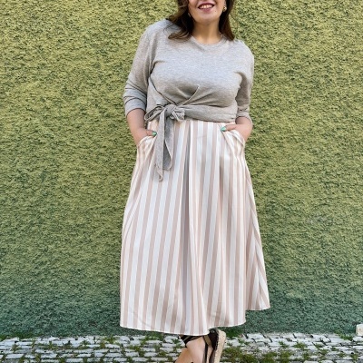 Mulher com camisola cinzenta e saia às riscas em fundo verde texturado