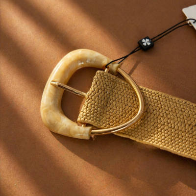 Cinto amarelo bege trançado com fivela de resina e metal dourado em superfície castanha