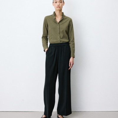 Mulher com camisa verde-oliva e calças largas pretas em fundo branco