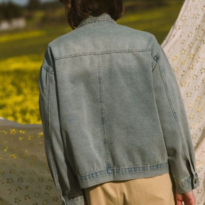 Casaco jeans azul claro visto de costas em ambiente exterior com flores amarelas