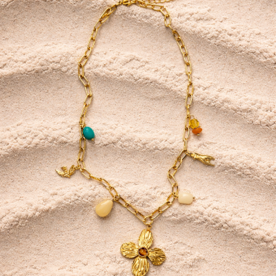 Colar dourado com flores e pedrinhas coloridas sobre areia