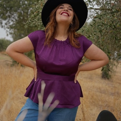 Mulher sorridente com blusa roxa e chapéu preto ao ar livre