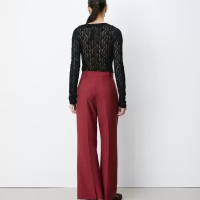 Pessoa de costas a usar blusa preta de renda e calças largas vermelhas