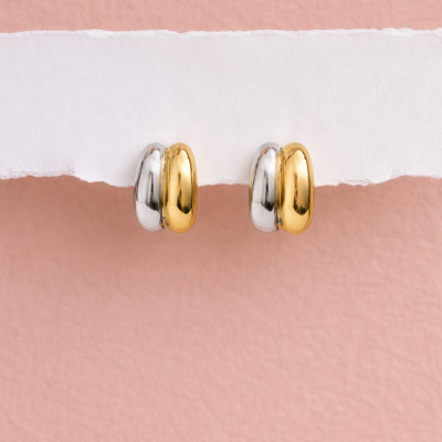 Brincos de argola bicolores em dourado e prateado sobre papel branco e fundo rosa