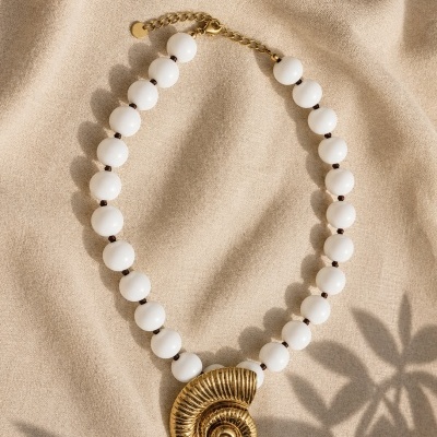 Colar de contas brancas com pendente dourado em espiral sobre tecido bege.