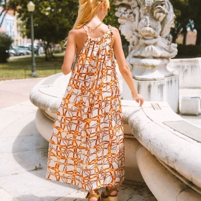 Vestido comprido com padrão castanho e branco e sandálias de plataforma, visto de costas junto a fonte de pedra