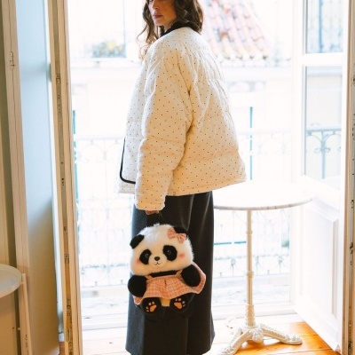 Bolsa peluche panda com vestido rosa e laço, mulher com casaco creme às bolinhas e calças cinzentas