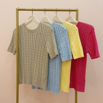 Quatro camisolas tricotadas de manga curta em várias cores penduradas num cabide.