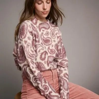 Mulher sentada com camisola felpuda rosa e branca e calças de veludo cotelê rosa.