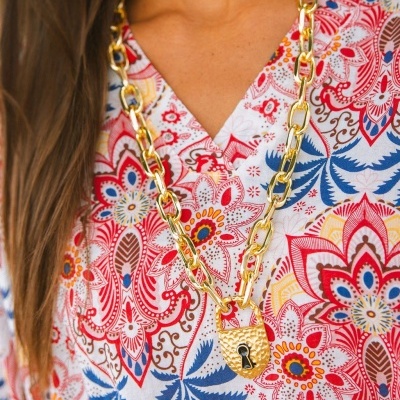 Colar dourado com cadeia grossa e cadeado pendente sobre blusa colorida com padrão floral