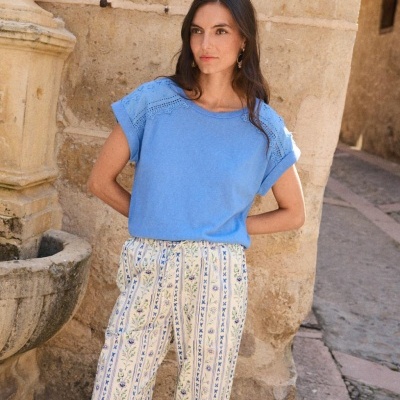 Mulher com camisola azul de renda e calças florais em ambiente histórico exterior
