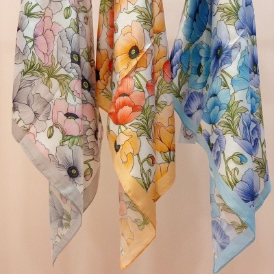 Três lenços florais coloridos pendurados em parede bege.