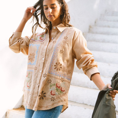 Camisa bege bordada com flores coloridas usada por mulher segurando casaco