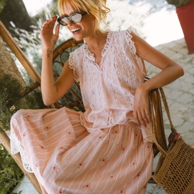 Conjunto feminino com blusa de renda branca e saia rosa de riscas e flores vermelhas.