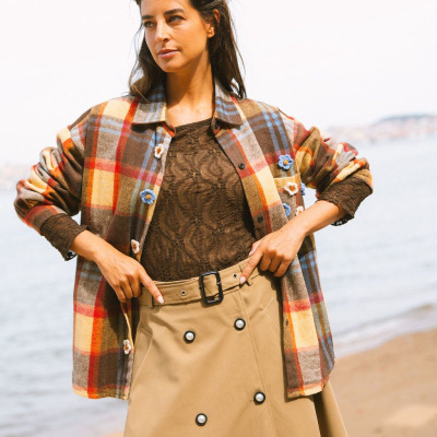 Mulher com camisa xadrez colorida e saia bege junto à praia.