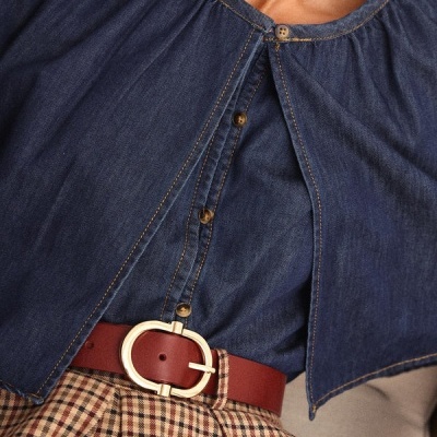 Blusa de ganga azul escura com botões castanhos e gola redonda, cinto vermelho com fivela dourada e saia xadrez