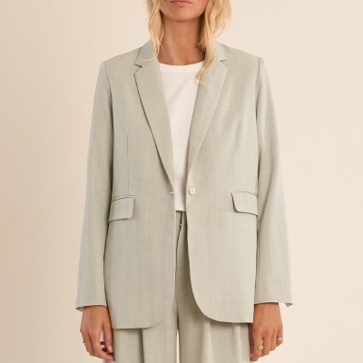 Fato feminino cinza claro com casaco e calças largas, t-shirt branca, em fundo neutro bege.