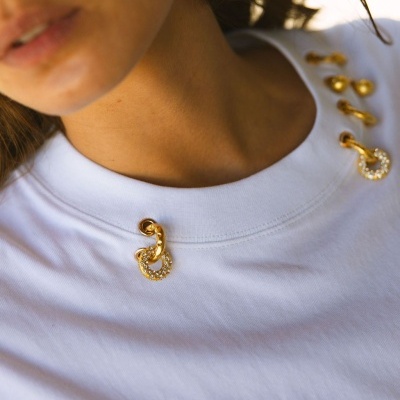 Detalhe da parte superior de uma t-shirt branca com botões dourados e pedraria