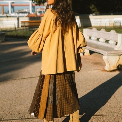Mulher com casaco amarelo oversize, saia xadrez castanha e botas bege em passeio ao ar livre