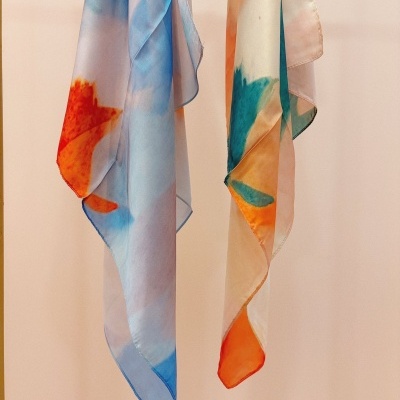 Duas echarpes coloridas penduradas contra fundo bege