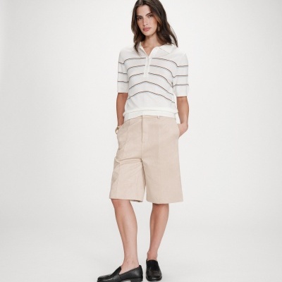 Mulher com camisola branca de malha fina com riscas horizontais e calções bege com sapatos pretos