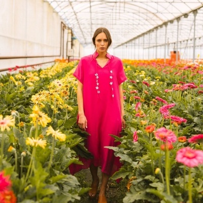 Mulher com vestido rosa fúcsia em estufa com flores amarelas e rosa.