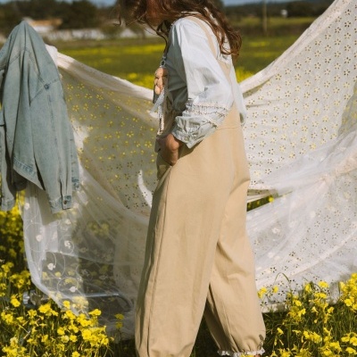 Macacão bege com camisa branca e ursinho de pelúcia em campo de flores amarelas