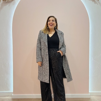 Mulher com casaco cinza de padrão espinha de peixe e calças largas pretas brilhantes