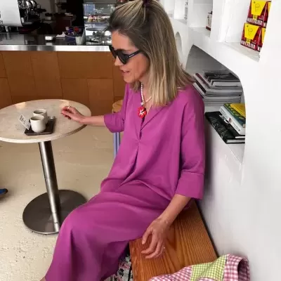 Mulher com vestido lilás e sapatos vermelhos sentada num banco numa cafetaria