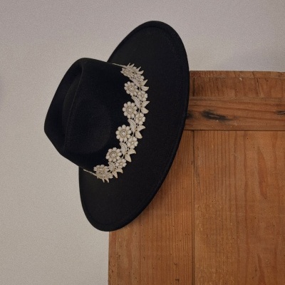 Chapéu preto com floral branco pendurado numa parede