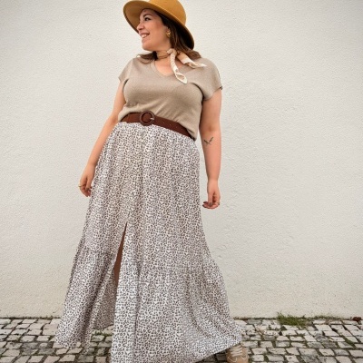 Mulher com roupa bege e castanha com saia animal print em calçada de pedra.